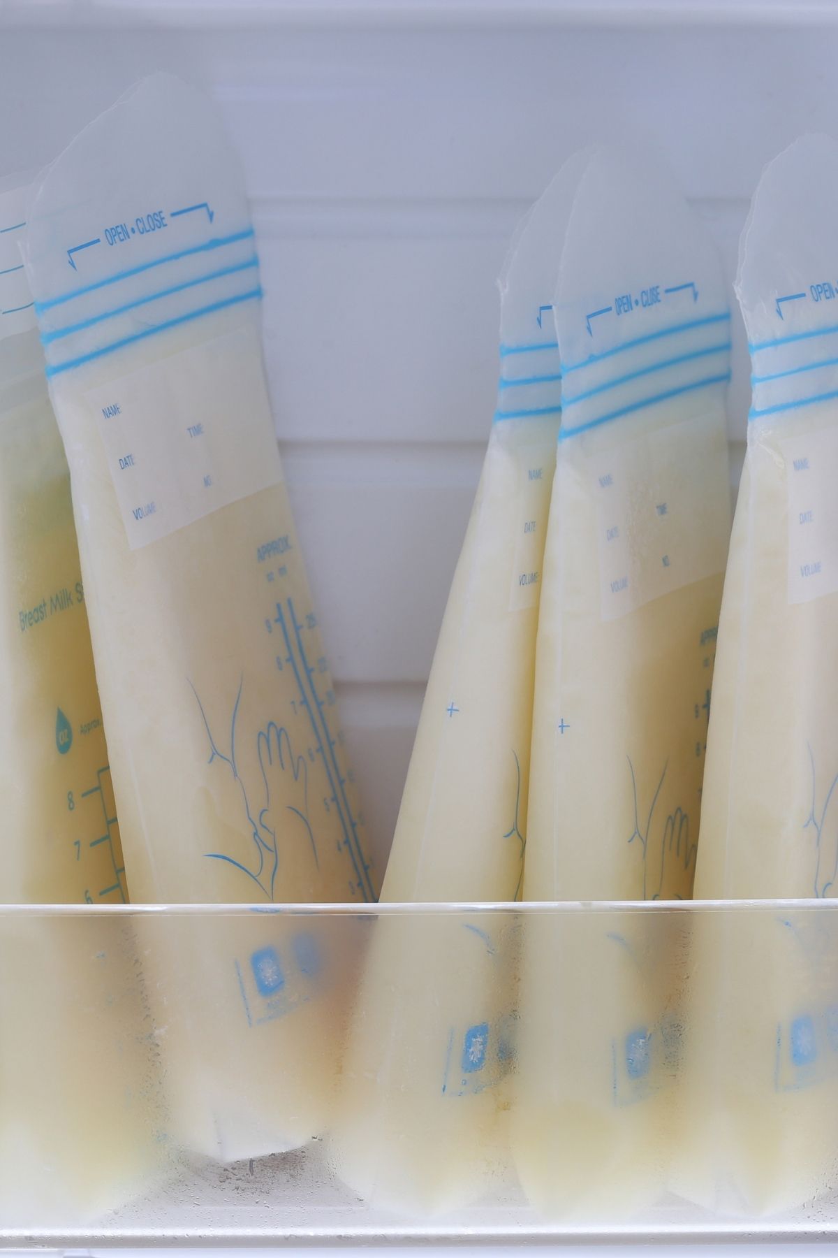 Several bags of frozen breast milk lined up inside a freezer shelf.
