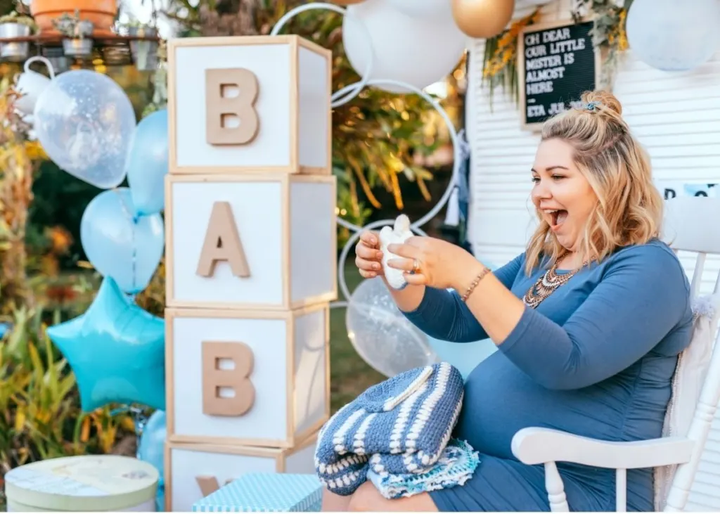 A woman opens baby shower gifts in an outdoor party setup.