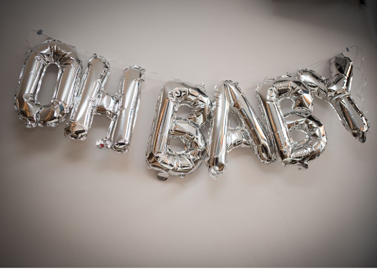 Silver balloons that say "Oh Baby" on a white wall.