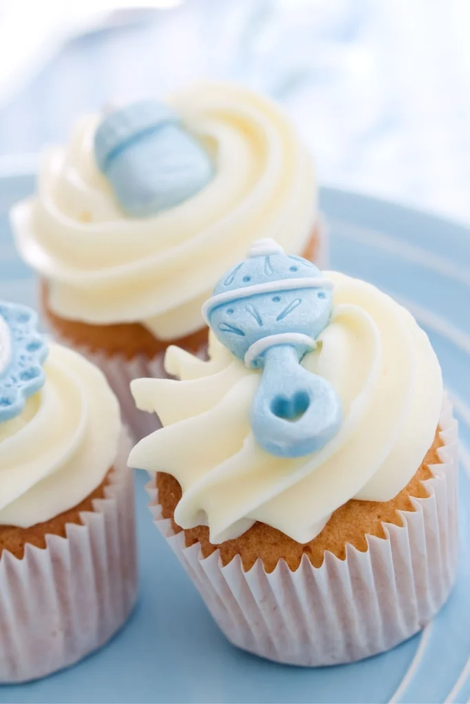 Cupcakes with white frosting and blue baby rattles on top.
