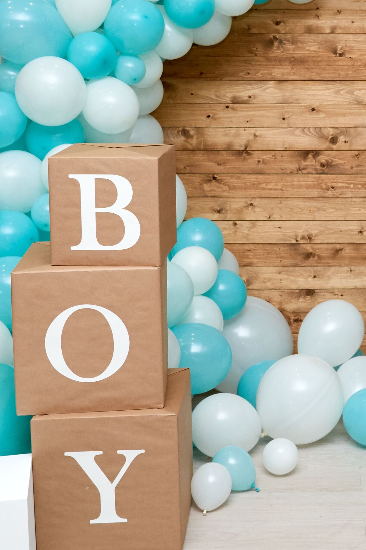 Boy spelled on three stacked boxes in front of a blue balloon arch.