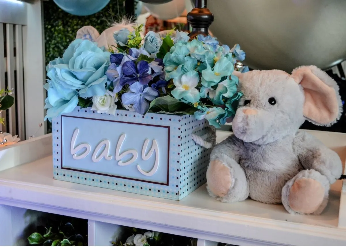 A blue flower arrangement in a box that says "baby" next to a stuffed elephant toy.