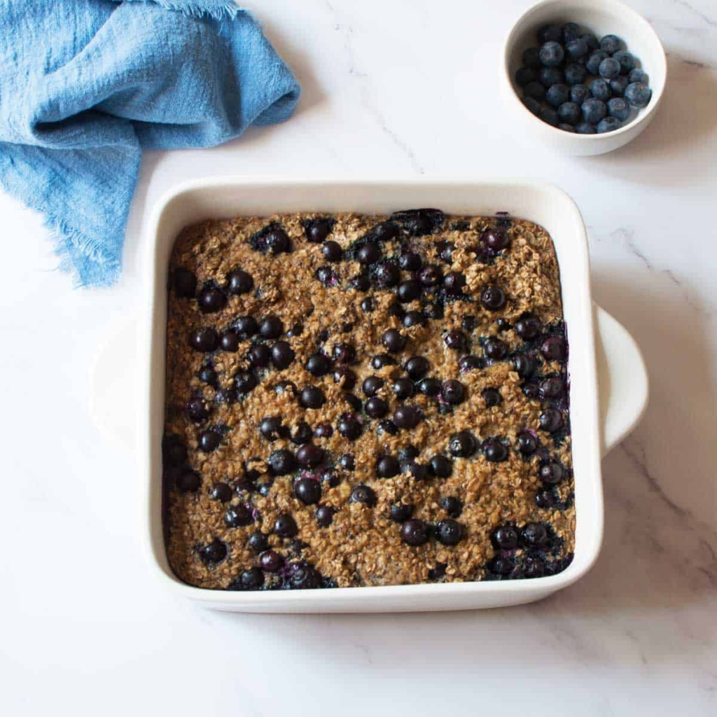 Baked oatmeal in a white square baking dish with blueberries.