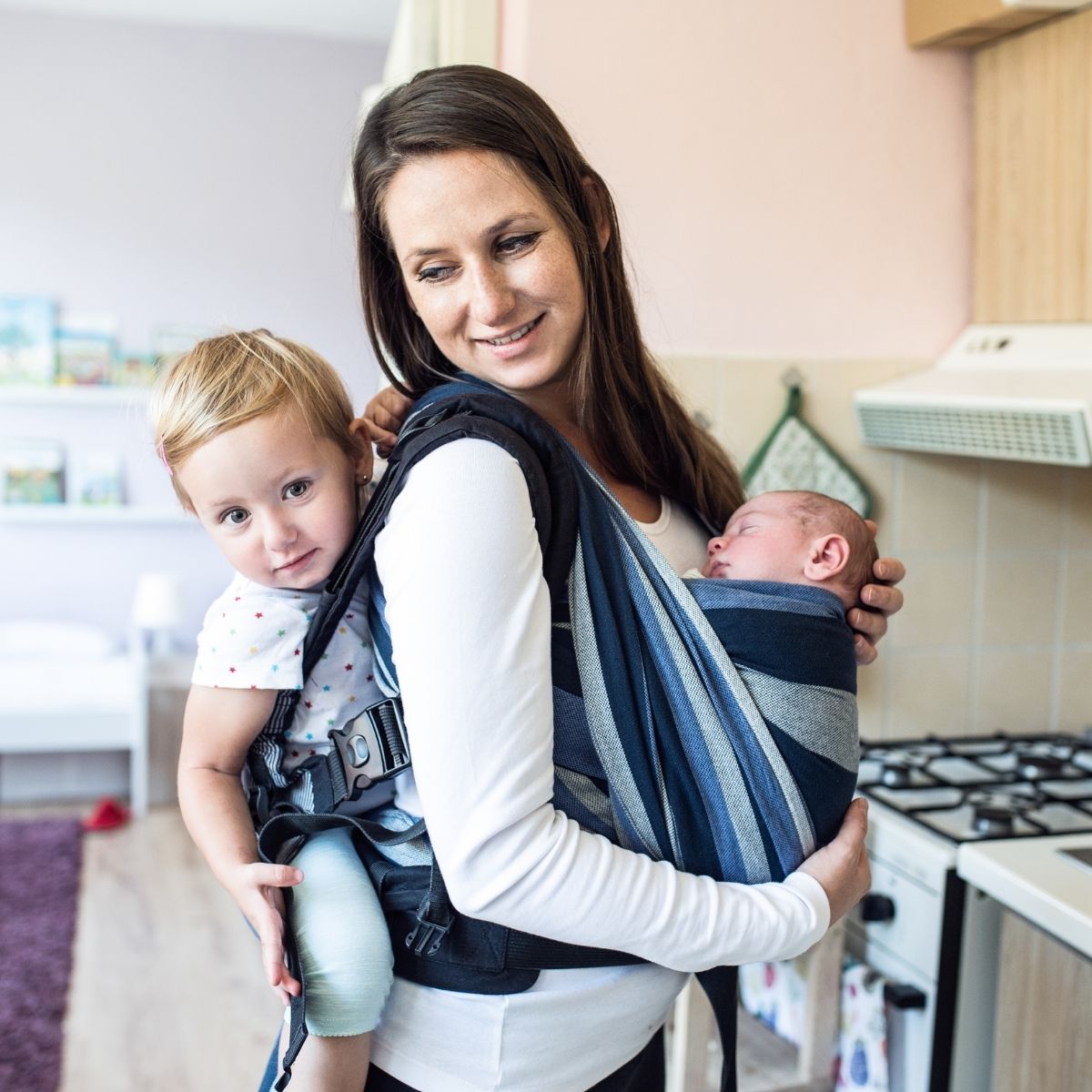 Mom wearing a baby and toddler in a sling and carrier.