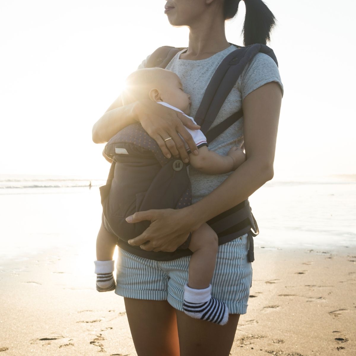 Mom with a baby in a carrier on the beach