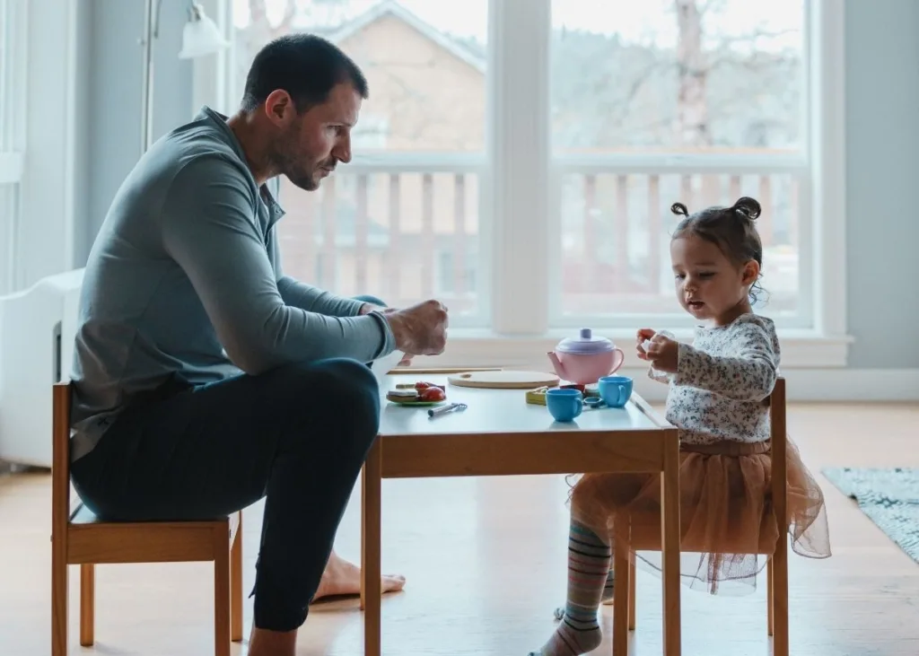 A daddy and daughter having a tea party at a small kid's table.