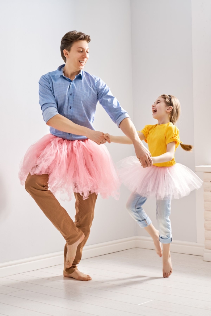A daddy and daughter dancing in tutus while holding hands.