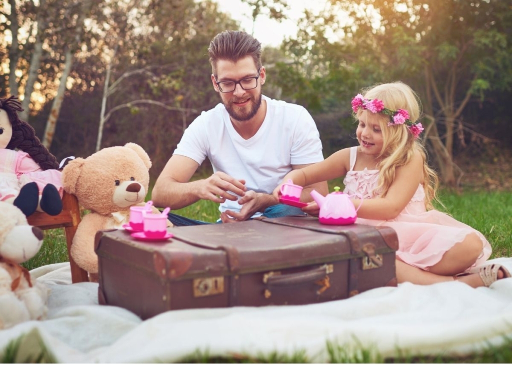 A dad and daughter having a picnic outside with a teddy bear.