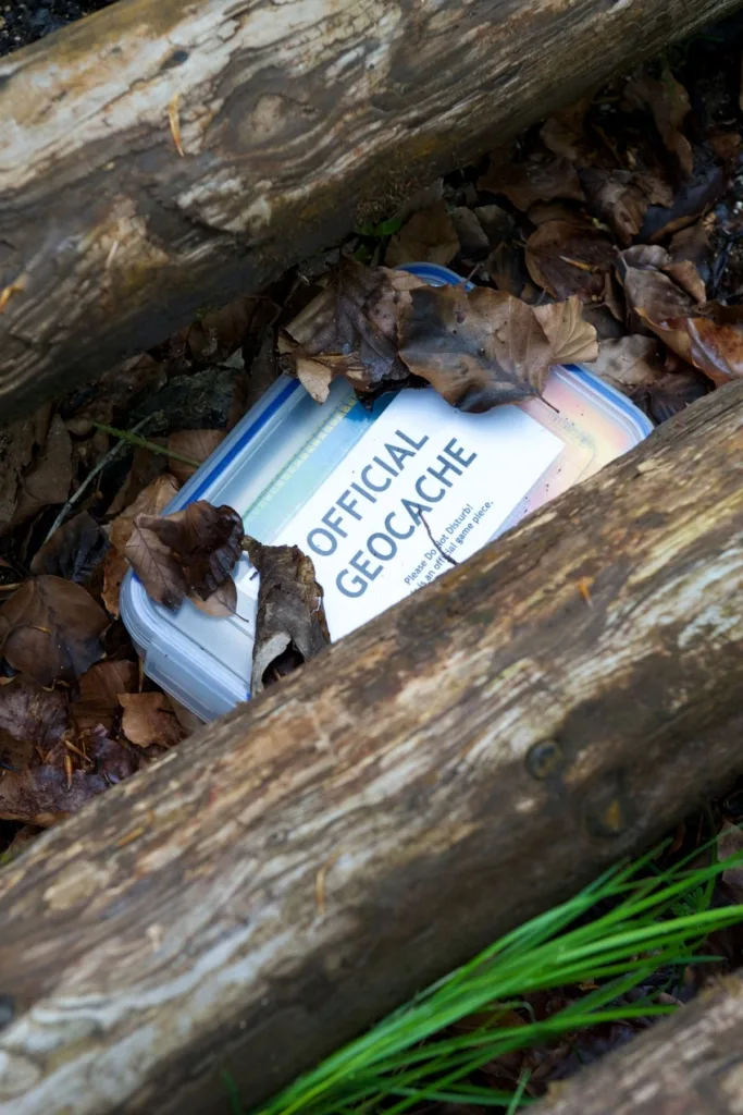 A box hidden under two logs with a label that says "Official Geocache".
