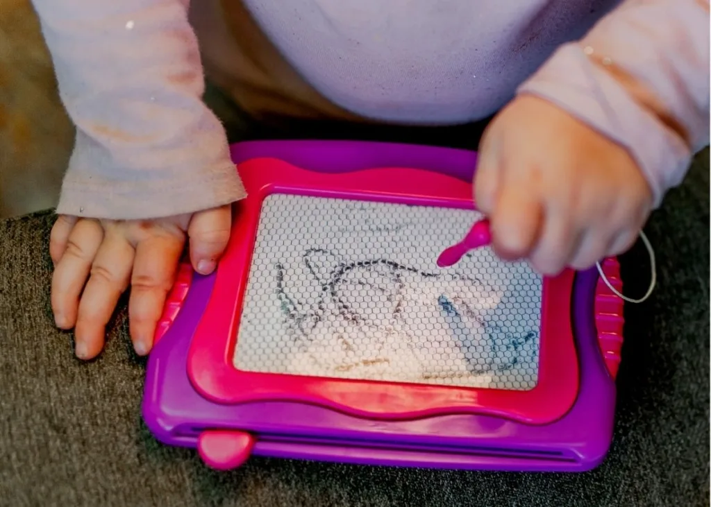 A toddler scribbles on a magnetic drawing tablet.