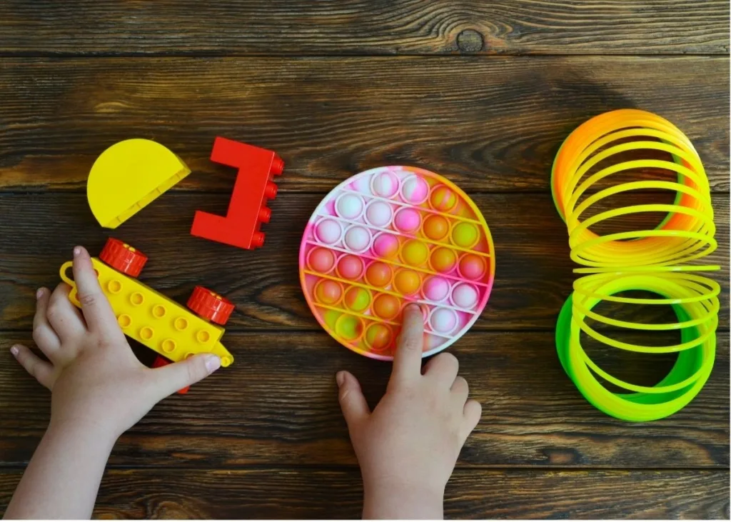 A toddler plays with Duplo blocks, a Pop-it, and a slinky.