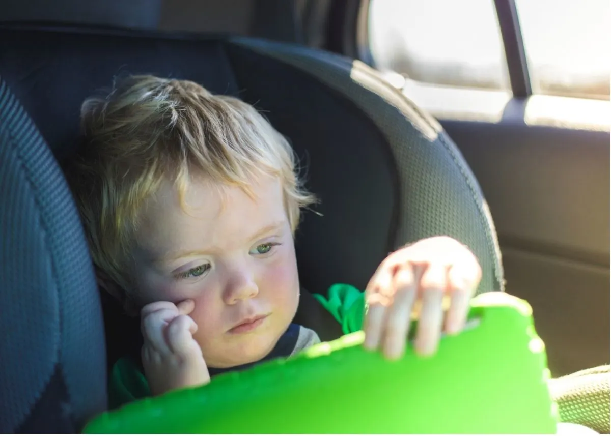 A toddler playing a green tablet in a car seat.