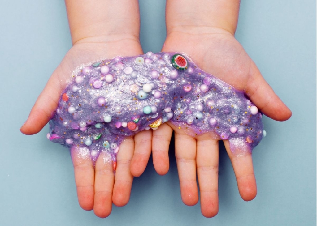 A toddler holds out purple slime with glitter.