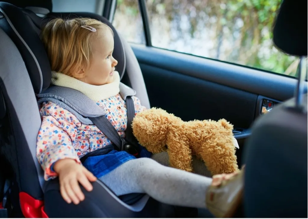 A toddler with a teddy bear in a car seat.