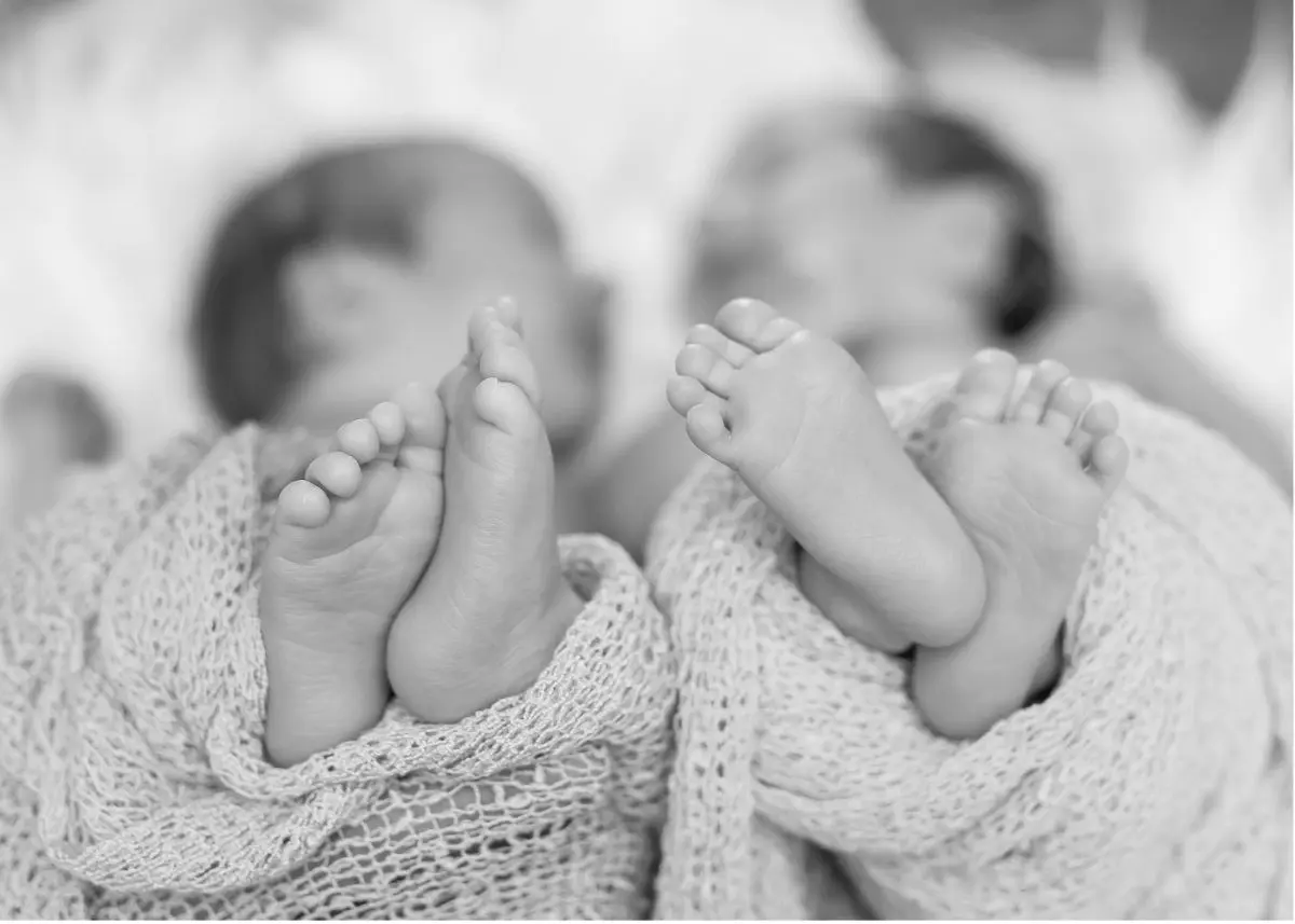 Black and photo photo of twin babies shot from the perspective of their feet.